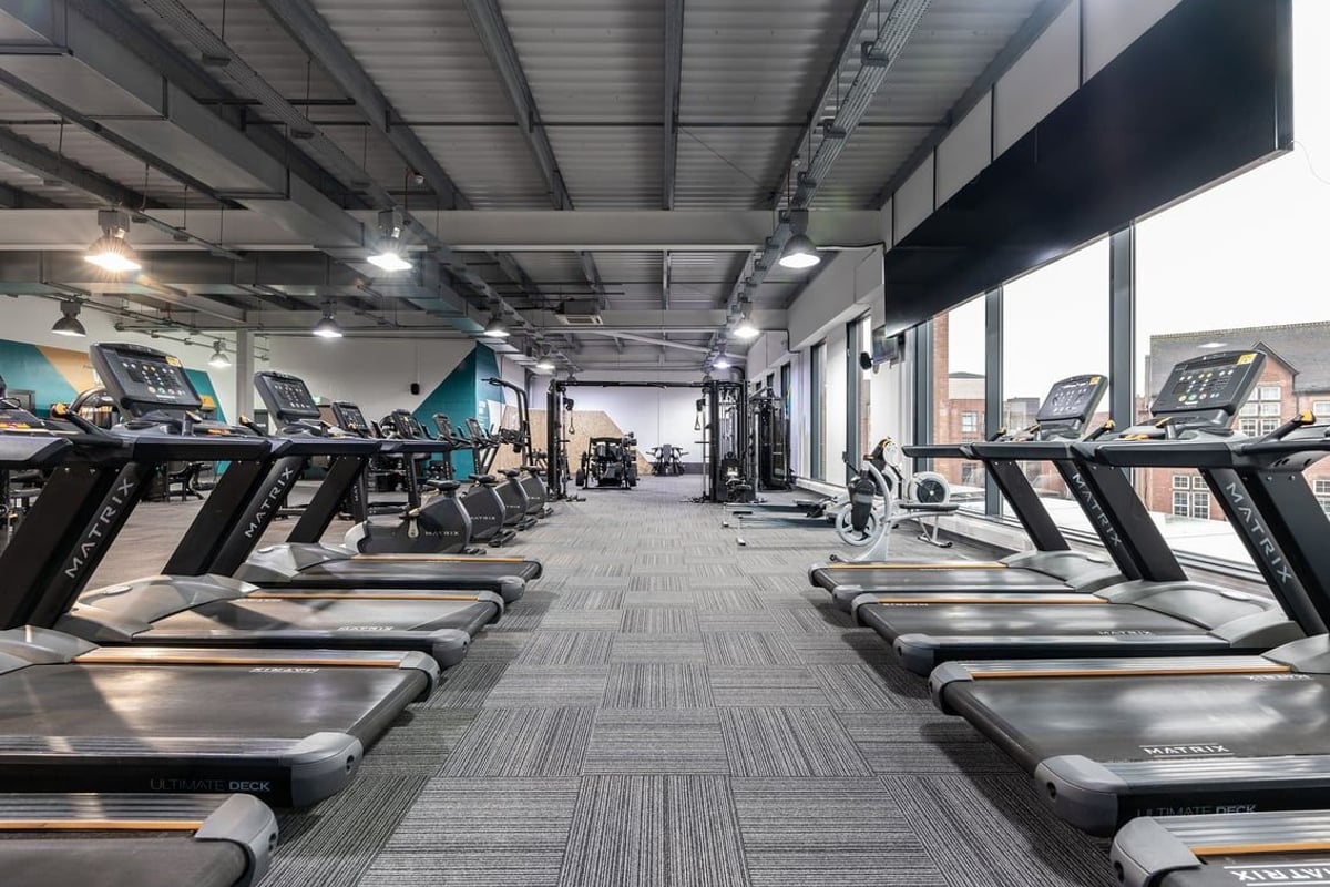 PureGym Nottingham Beeston: Rows of treadmills, weight machines and free weights in a brightly lit gym studio with mirrors.