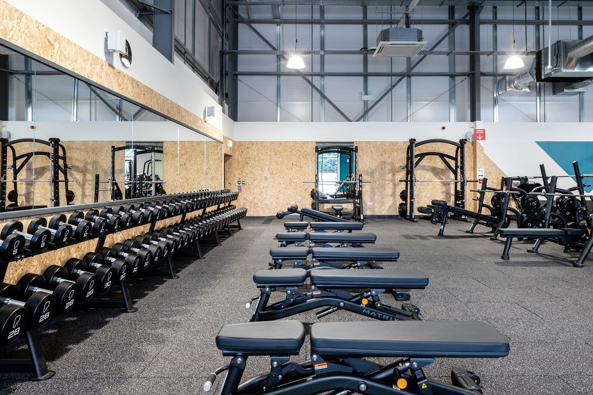 PureGym Cirencester: Rows of weight benches, dumbbells and weights machines in a gym setup.