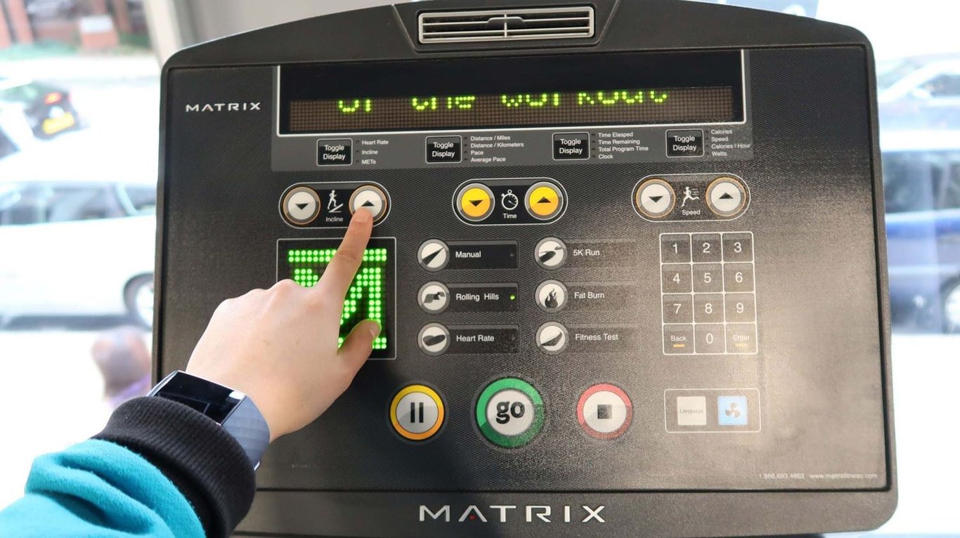 Hand pressing incline up button on treadmill control panel with various settings and butto