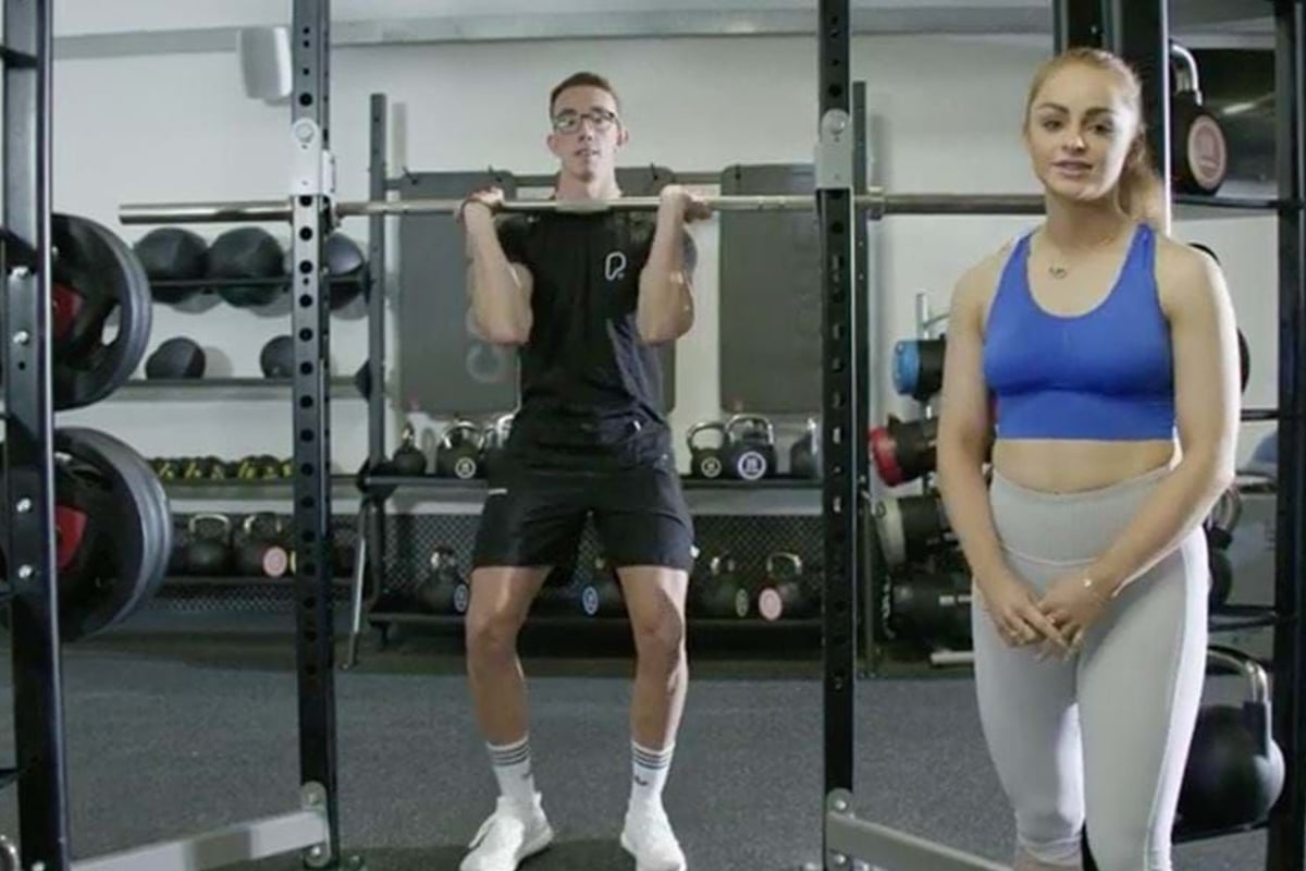 Man lifting barbell while woman in sportswear stands beside him in gym