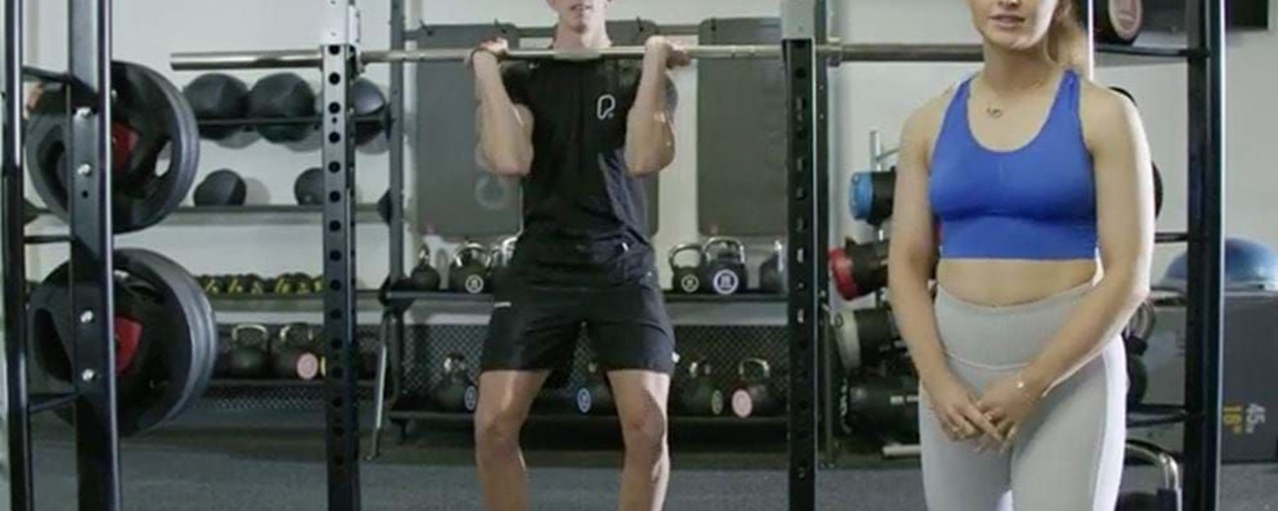 Man lifting barbell while woman in sportswear stands beside him in gym