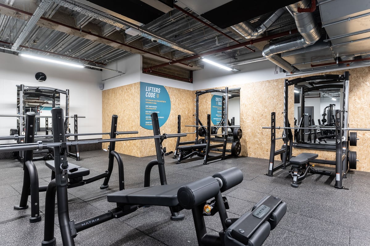 PureGym London Monument: Weight racks, benches, mirrors, rubberised flooring in a gym setting with visible ductwork.