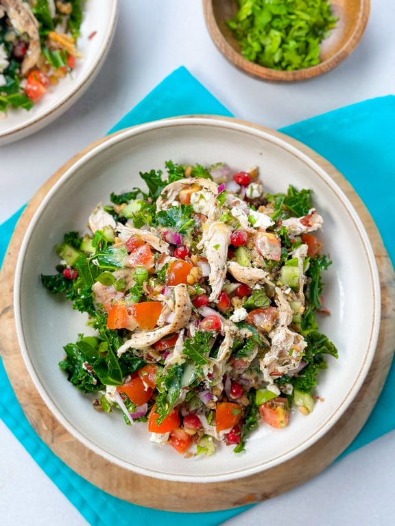 Bowl of mixed salad with shredded chicken, kale, tomatoes, cucumber, and pomegranate seeds