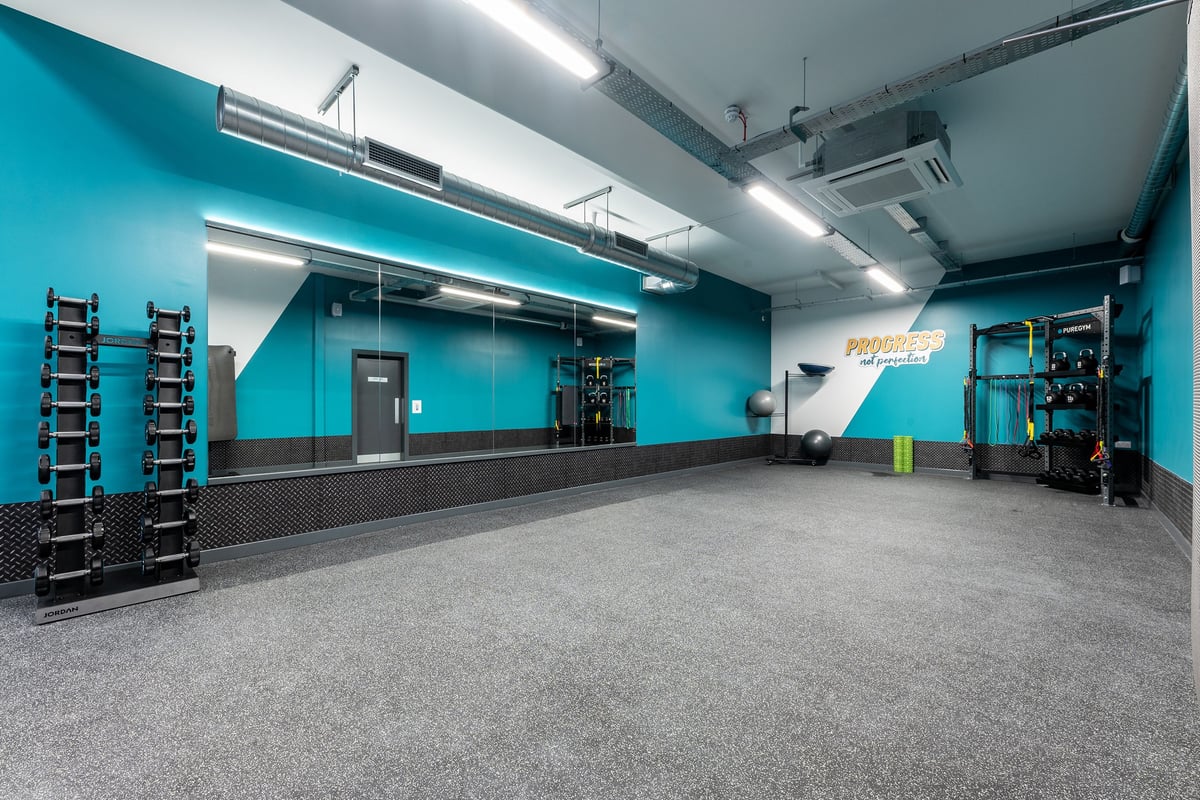 PureGym Blyth: Turquoise studio with weight racks, dumbbells, exercise machines, and rubberized floors.
