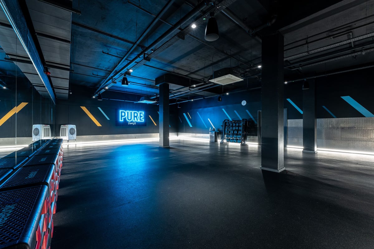 PureGym London Hammersmith Palais: Large open space with blue lighting, padded floors, and punching bags by the wall.