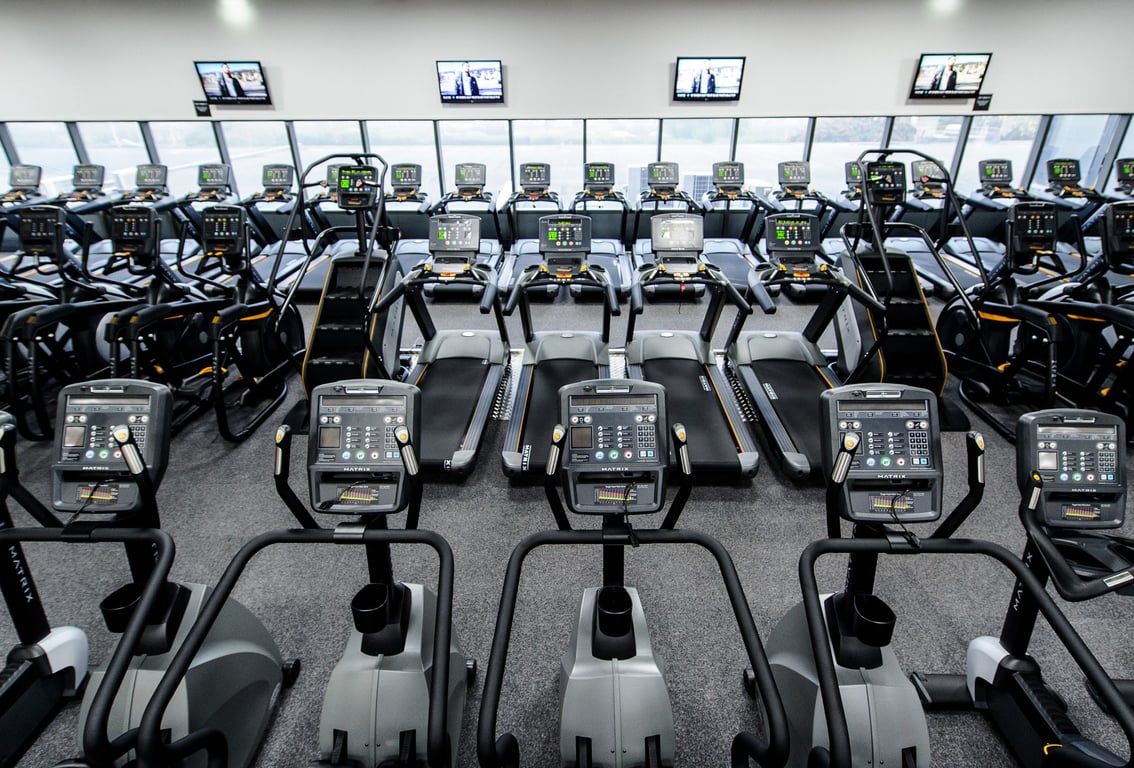 PureGym Bedford Heights: Rows of treadmills facing TV screens in a gym's cardio training area.