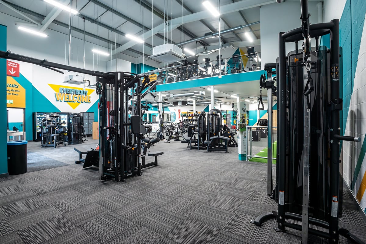 PureGym Market Harborough: Weight machines, free weights, turf area, and patterned rubberized flooring in a brightly lit gym.