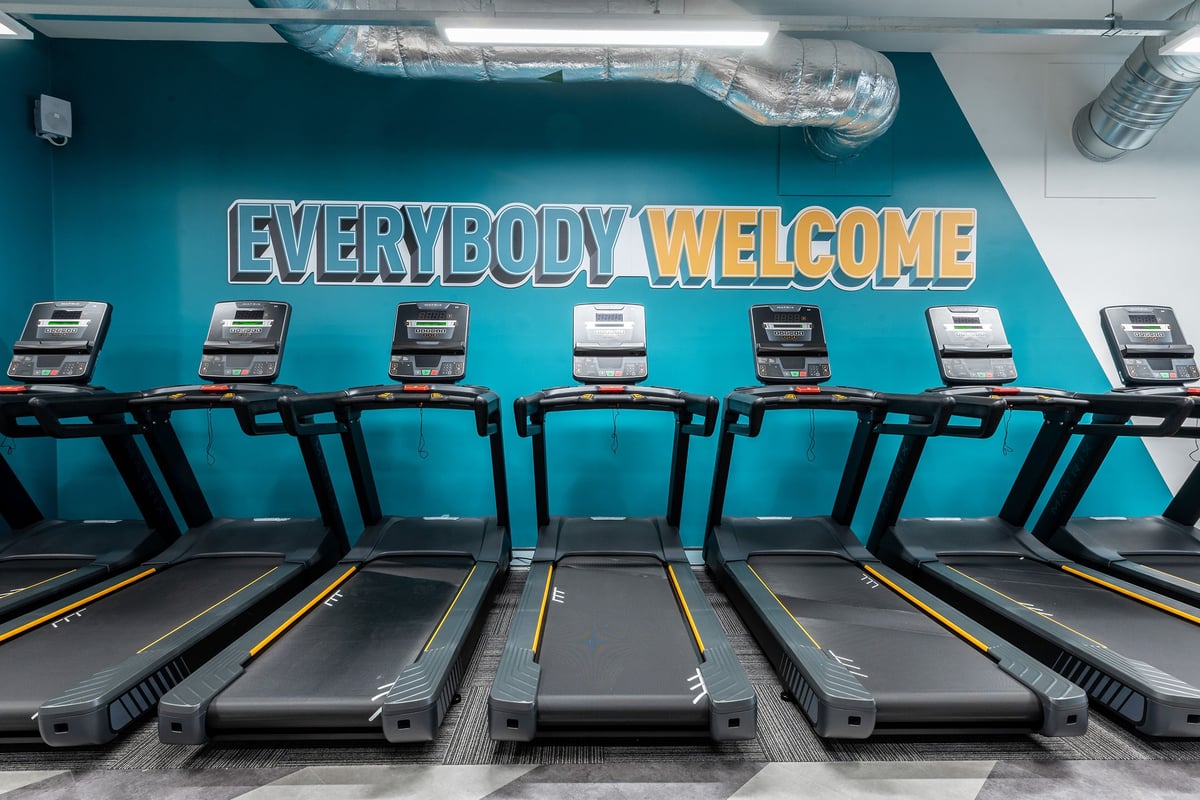 PureGym Milton Keynes Kingston Centre: Rows of treadmills with a large "EVERYBODY WELCOME" sign on the teal-coloured wall.