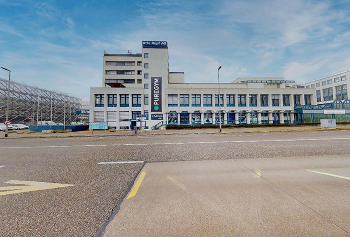 Puregym Dübendorf: Fassade eines Geschäftshauses mit Parkplatz davor.