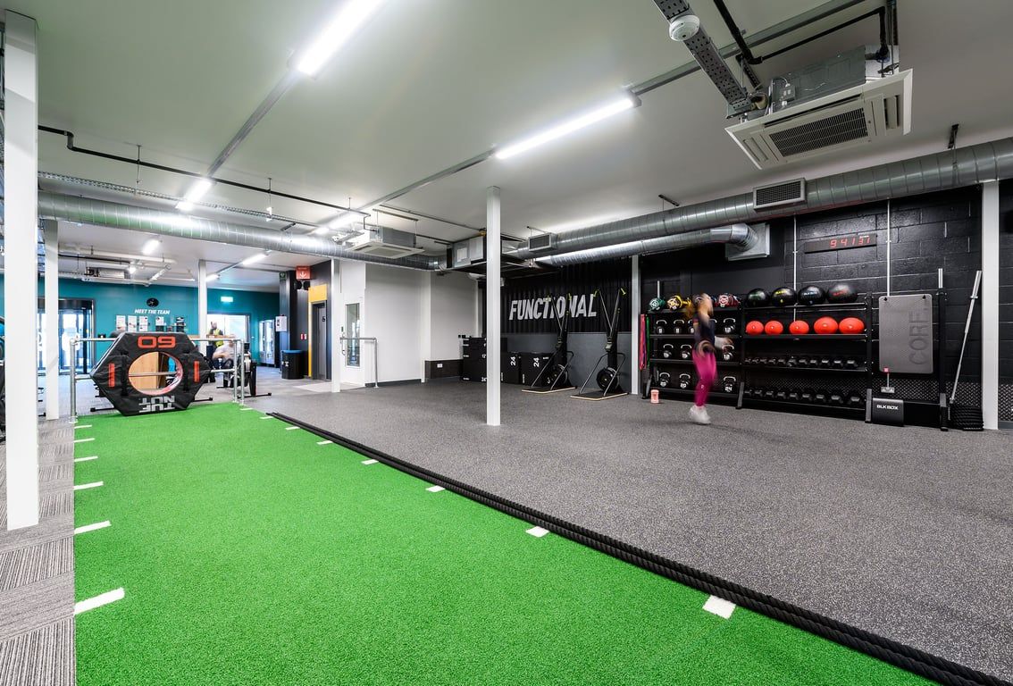 PureGym St Albans: Functional training area with green turf, freeweights, exercise balls, and mirrored walls.
