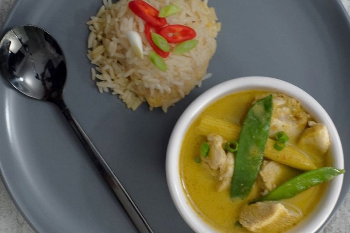 Bowl of yellow curry with chicken and mangetout beside mound of rice