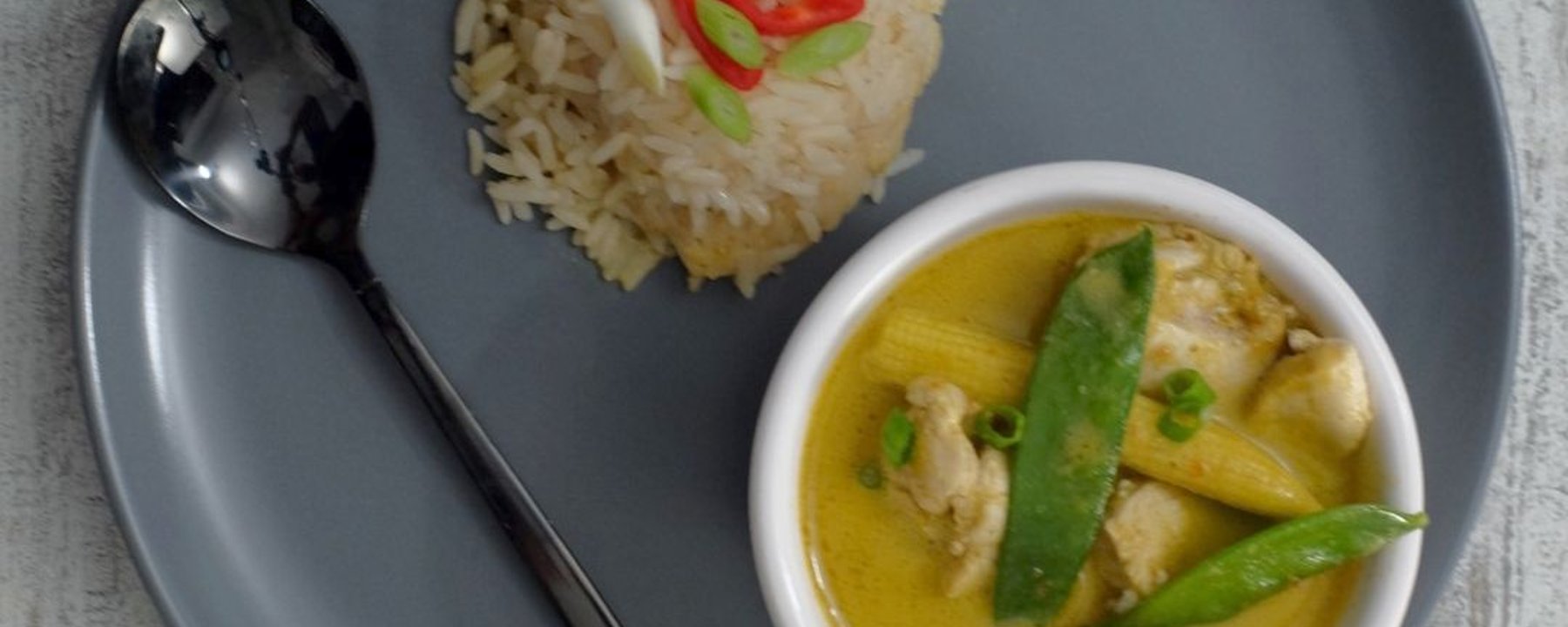Bowl of yellow curry with chicken and mangetout beside mound of rice