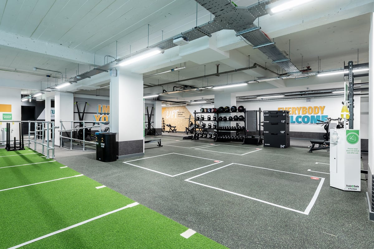 PureGym London Holloway Road: Gym studio with turf area, weight racks, benches, resistance machines, and mirrored walls.