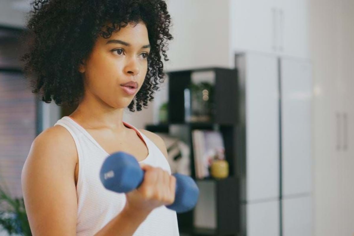 Woman lifting a blue dumbbell in a white tank top in a modern kitchen