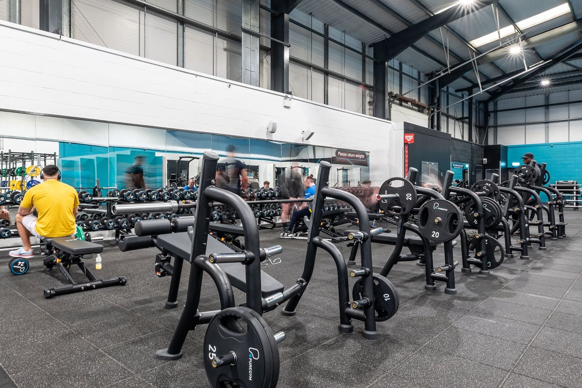 PureGym Leeds Hunslet: Rows of stationary exercise bikes and weight stands on rubberised gym floor.