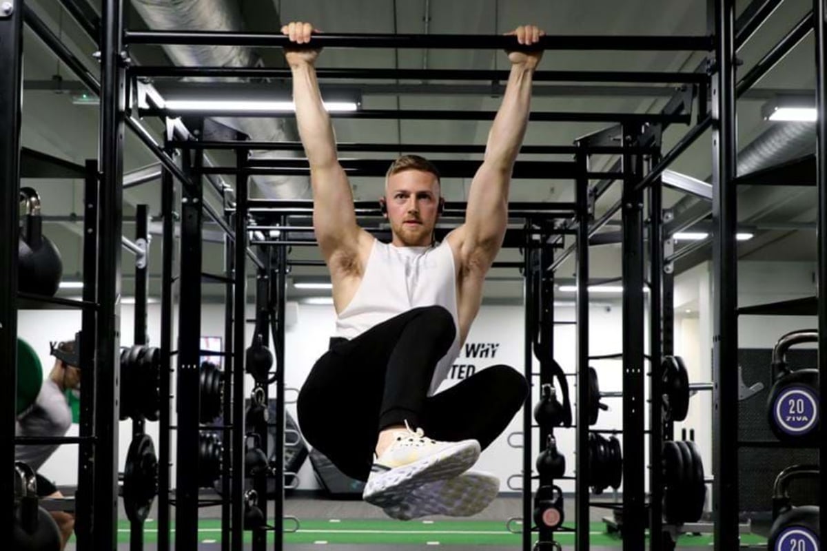 Man in white vest doing hanging leg raises on pull-up bar in gym