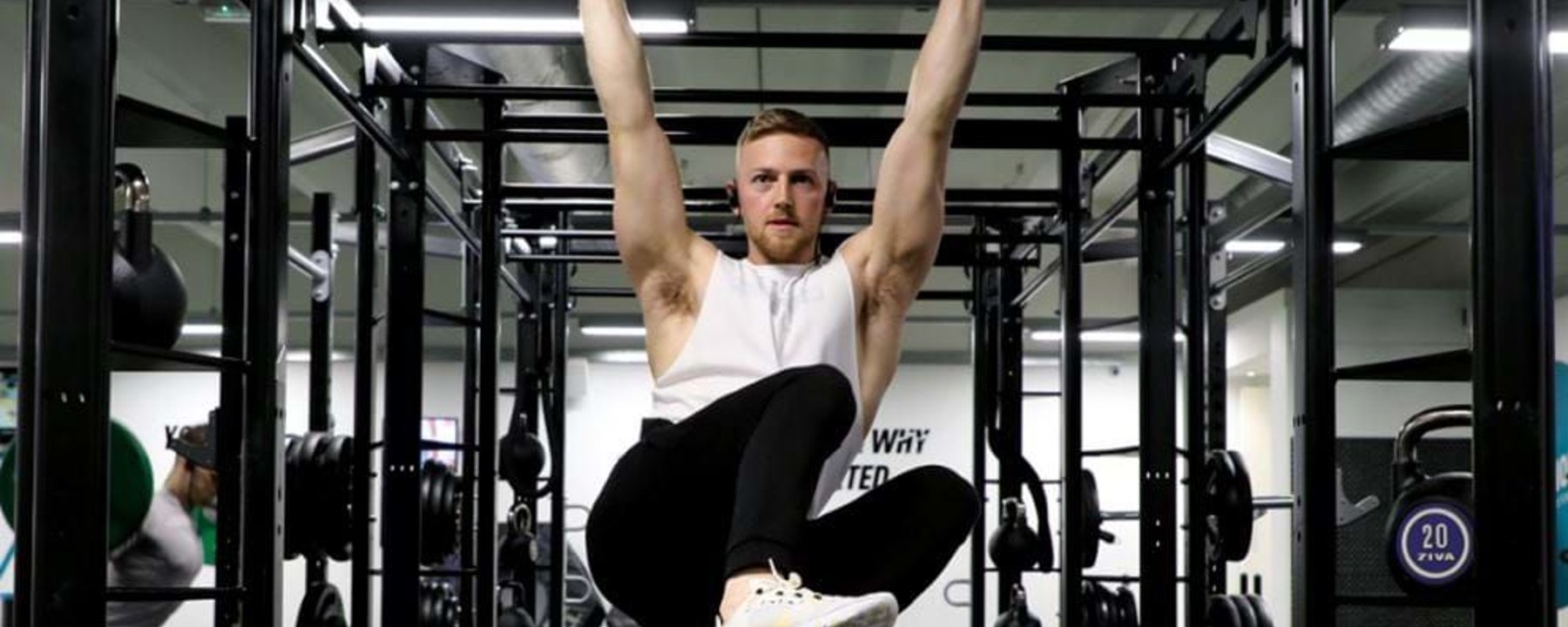 Man in white vest doing hanging leg raises on pull-up bar in gym