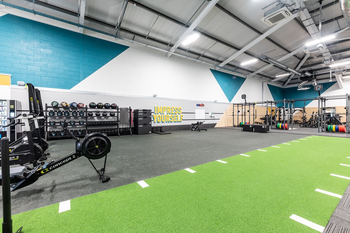 PureGym Ballymena: Weight racks, resistance machines, turf area, industrial interior with blue and white walls.