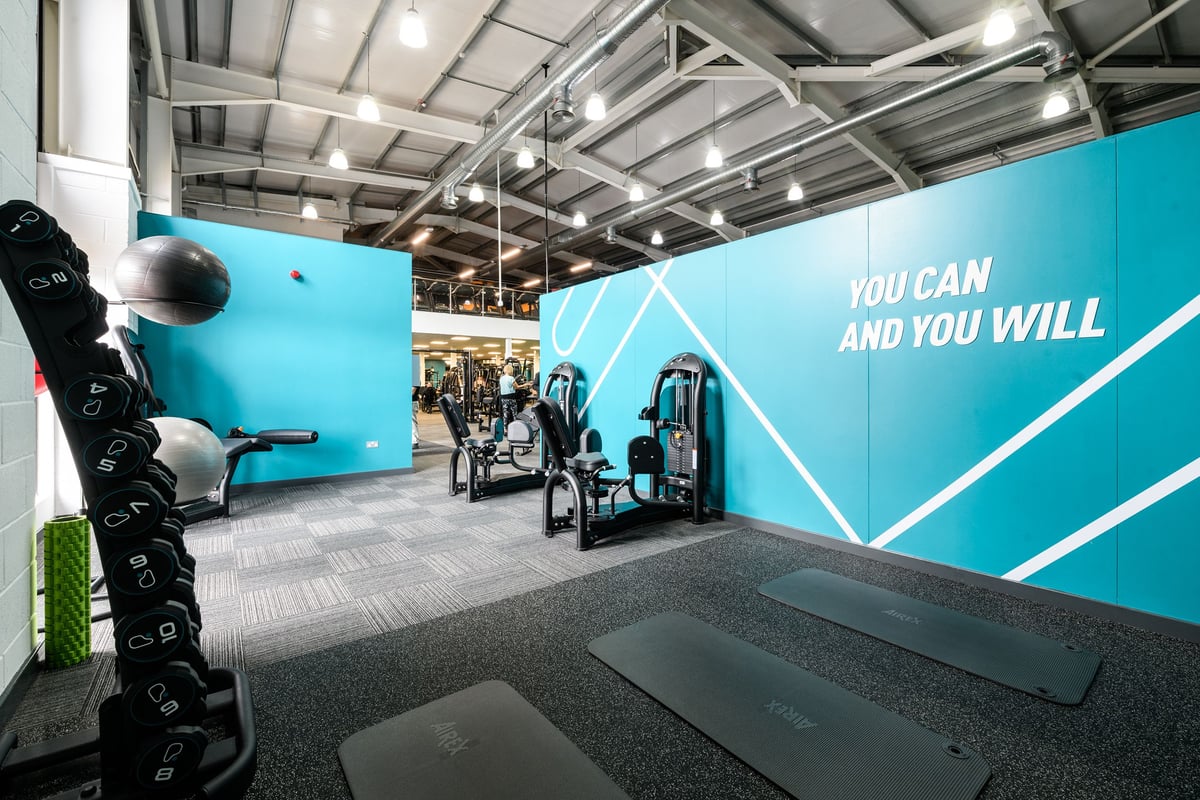 PureGym Lichfield: Resistance machines, weights, rubberized floor, motivational wall graphics in teal and white.