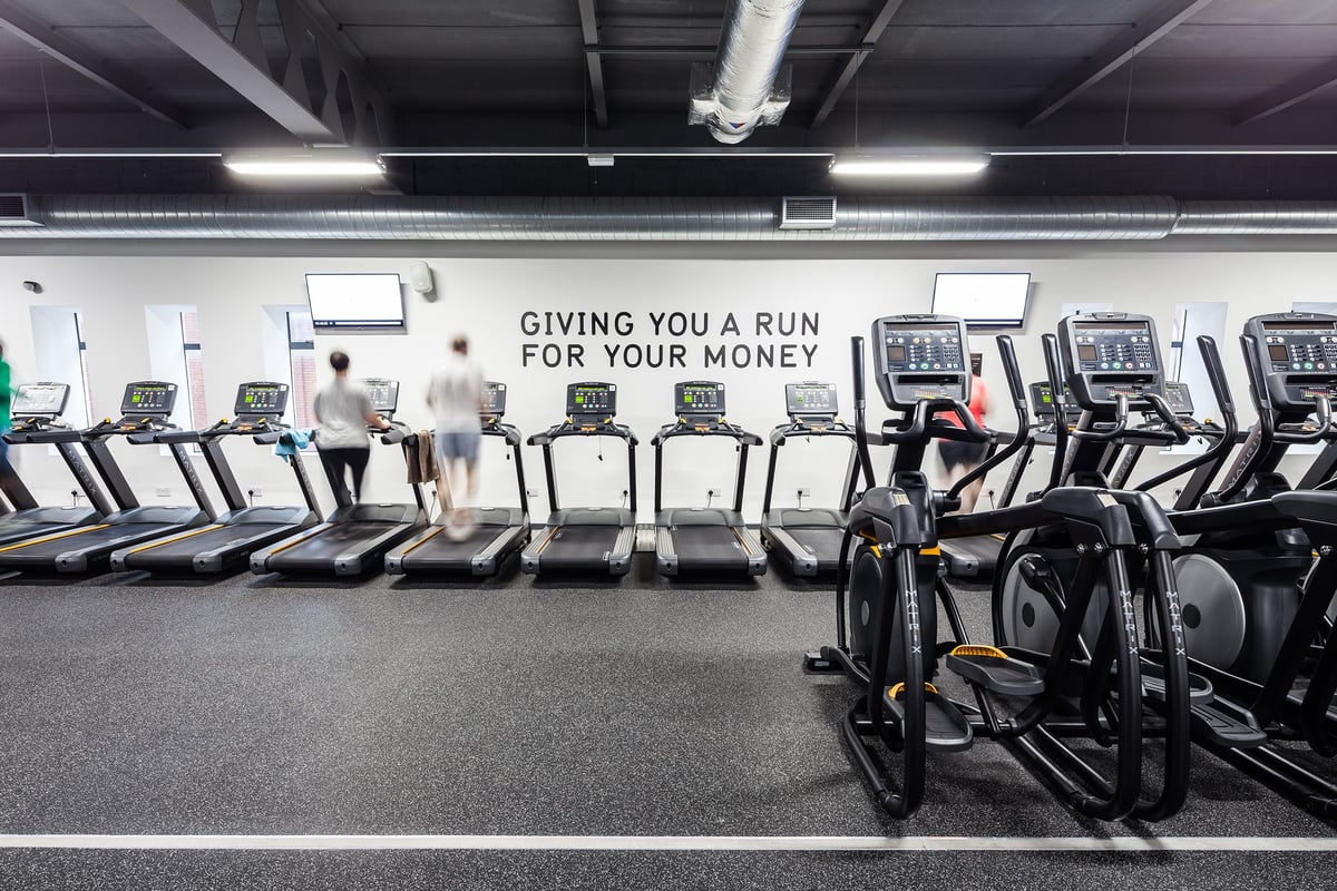 PureGym Manchester Stretford: Rows of treadmills with digital displays and a motivational slogan on the wall.