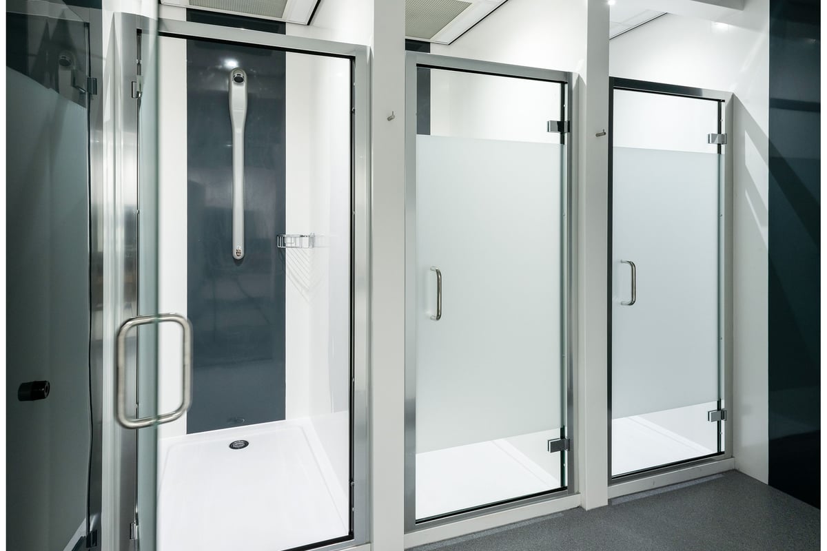 PureGym Cannock Orbital Retail Park: Rows of shower stalls with glass doors and brushed metal fixtures.