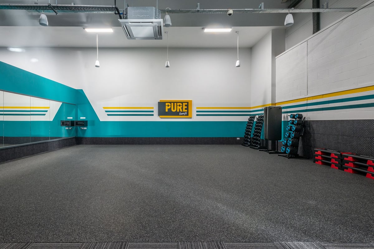 PureGym Oswestry: Grey rubberized floor, blue and yellow striped walls, weight racks, PURE signage.