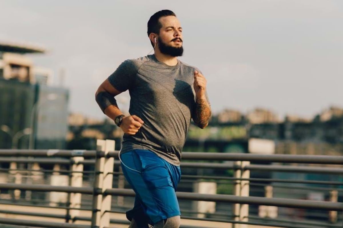 Man with beard and tattoos jogging outdoors near metal railings in cityscape background