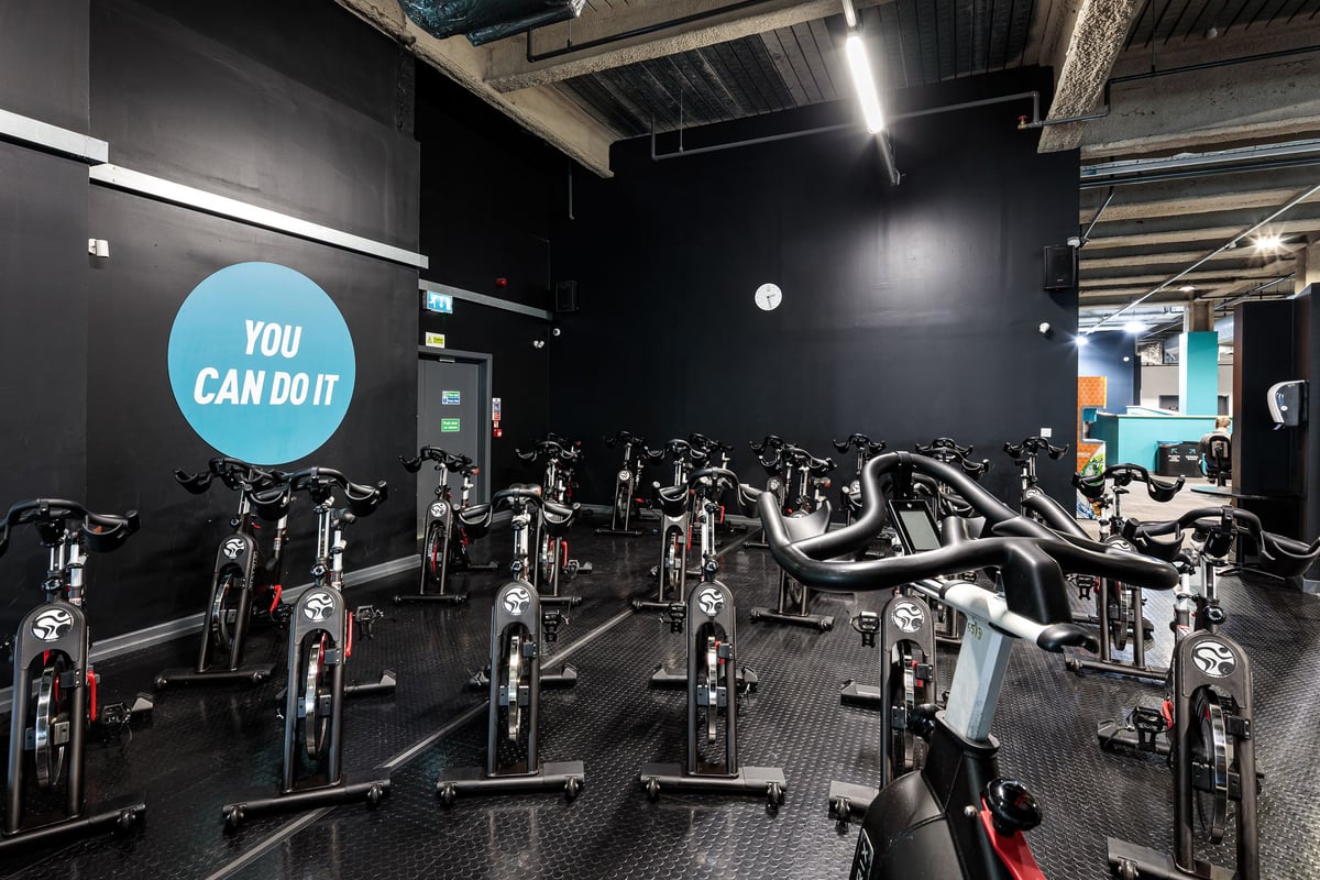 PureGym Cardiff Central: Rows of stationary bikes, motivational signage, and sleek black studio interior.