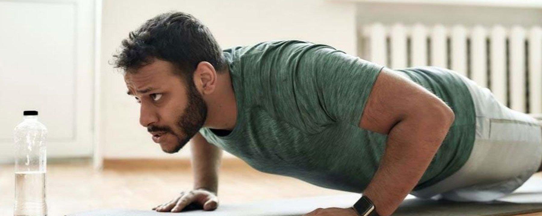 Homme en chemise verte faisant des pompes sur un tapis avec une bouteille d'eau à côté