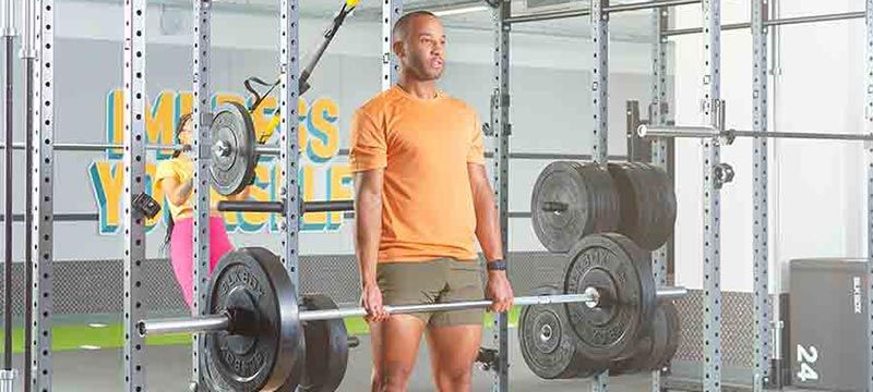 Mann im orangefarbenen T-Shirt hebt Langhantel im Fitnessstudio mit Gewichten.