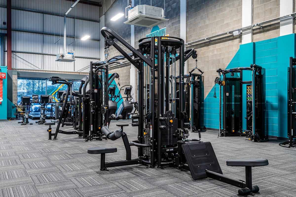 PureGym Elgin: Rows of cable machines, weight racks, benches and mirrors in a gym floor setting.