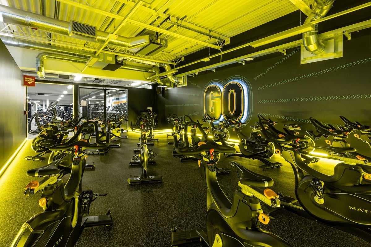 PureGym Motherwell: Rows of stationary bikes, treadmills, weights, benches in a dimly lit yellow-tinted fitness studio.