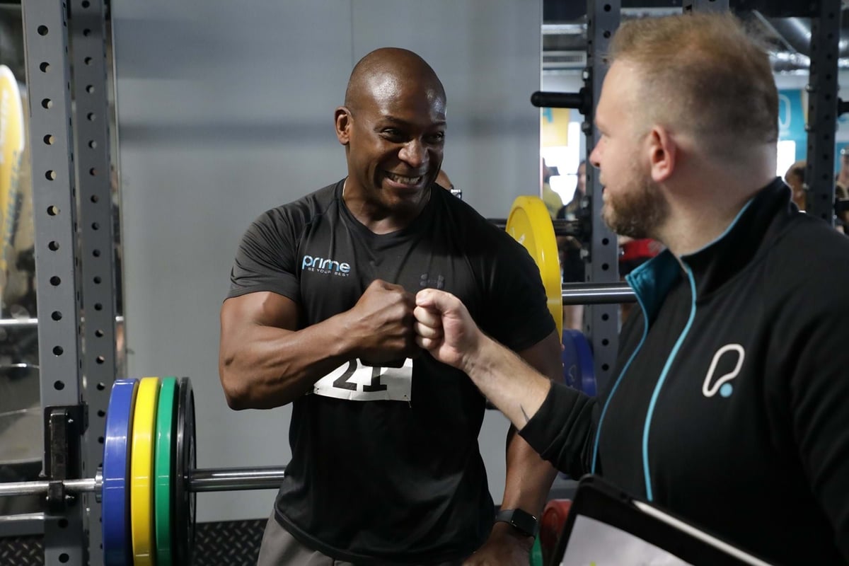 Two men fist bumping in a gym with weightlifting equipment in the background