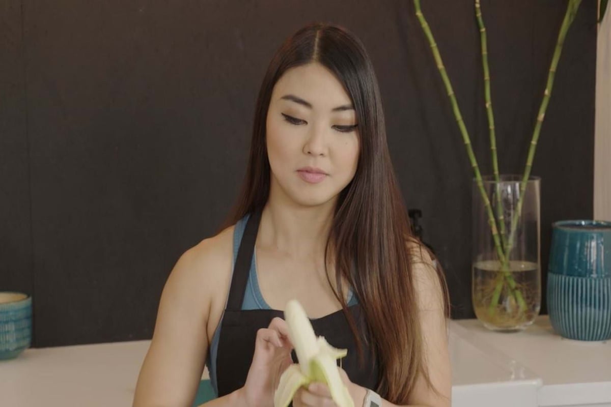Woman peeling a banana in a kitchen with bamboo stalks in a glass vase behind her