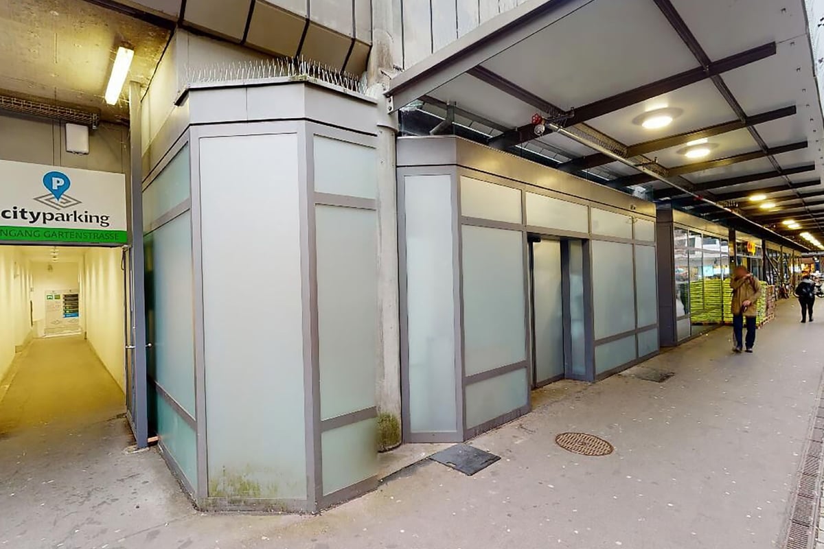 PureGym Biel Bienne: Passerelle couverte avec portes d'entrée au parking, éclairée par le haut par un éclairage fluorescent.