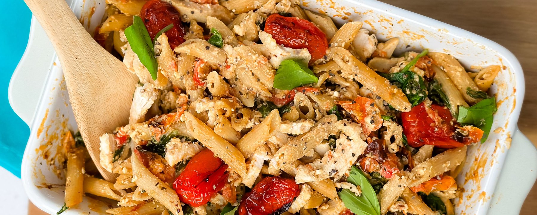 Pasta with tuna, roasted red peppers, spinach and cheese in white baking dish