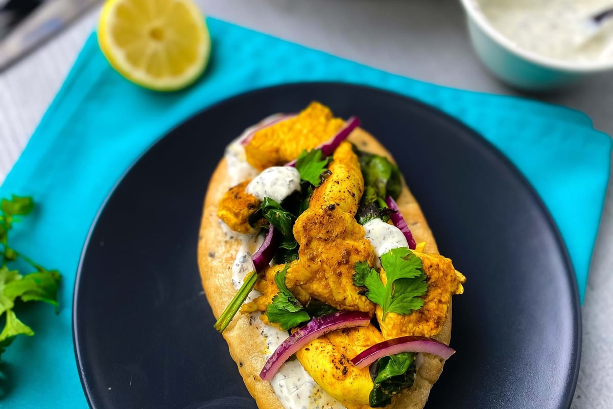 Flatbread topped with grilled chicken, sauce, red onions, and fresh herbs on a black plate