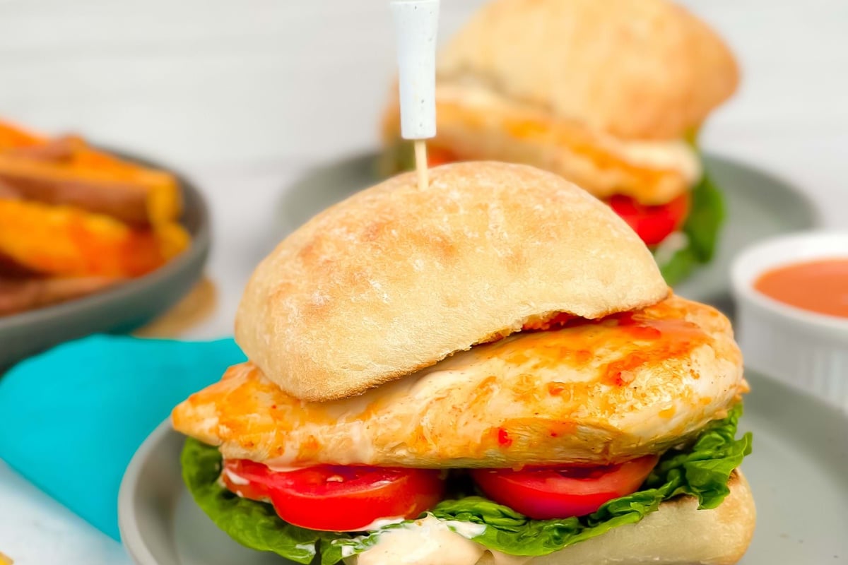 Grilled chicken sandwich with lettuce and tomato on a grey plate with a blue napkin.