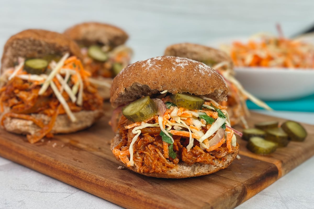 Pulled pork burgers with coleslaw and pickles on a wooden board beside a bowl of slaw