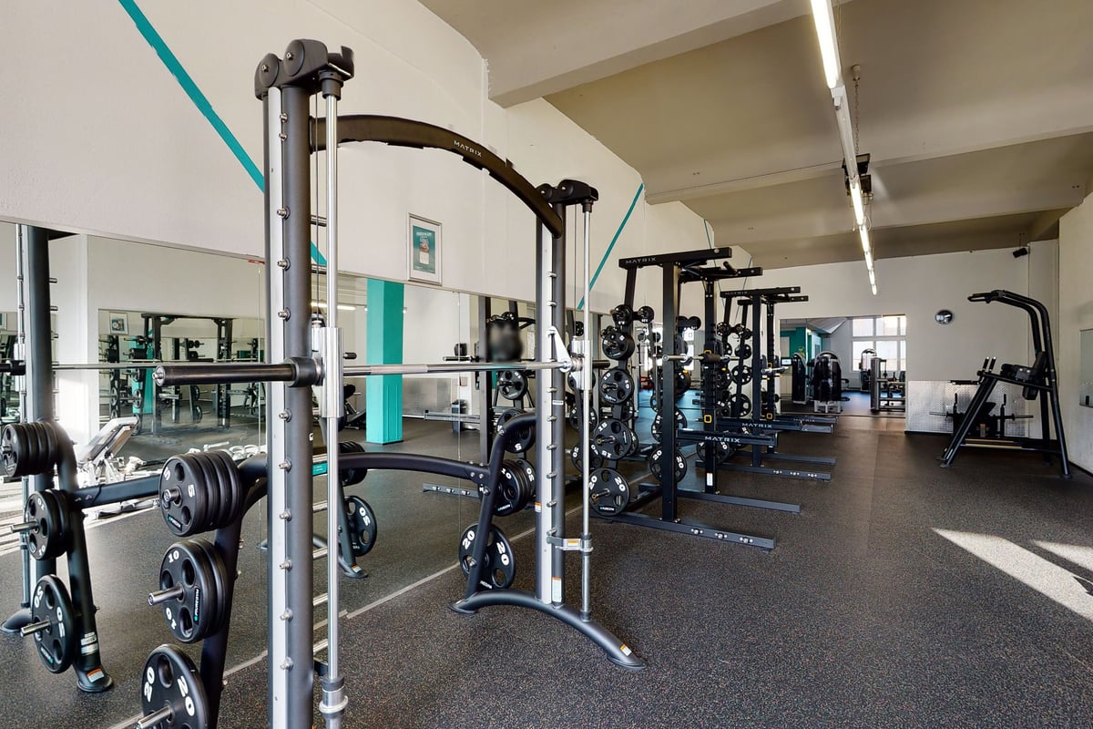 PureGym Rorschach: Salle de sport avec équipement de musculation, supports de squat, bancs, sols caoutchoutés et touches bleu sarcelle.