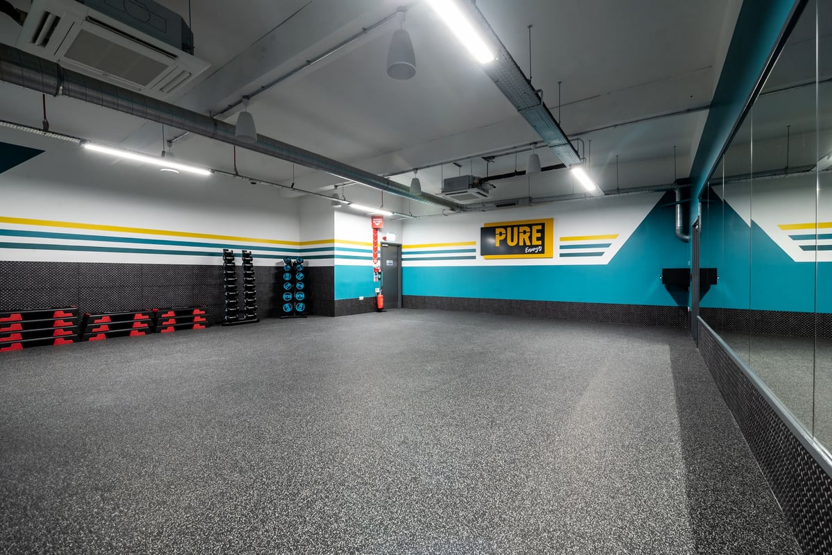 PureGym London Bethnal Green: Rubberized flooring, free weight stands, weight plates in vibrant colours, mirrored wall.