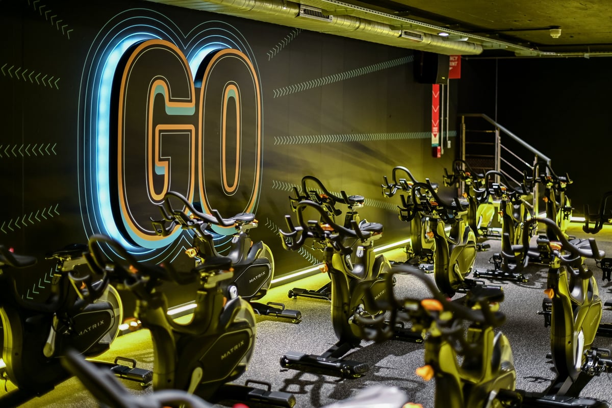 PureGym London Piccadilly: Rows of stationary bikes, neon "GO" signage, industrial lighting and design aesthetic.
