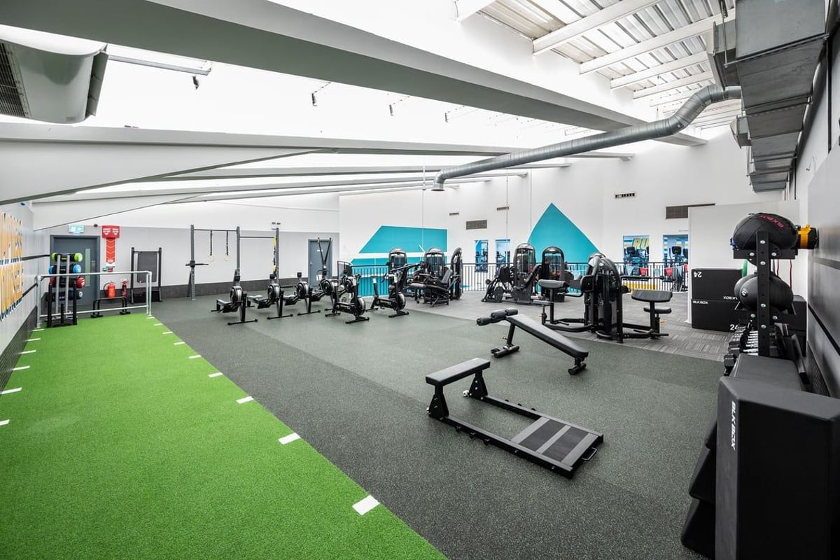 PureGym Belfast Boucher Road: Weight racks, benches, turf area, mirrors, and exercise equipment in a gym studio setting.
