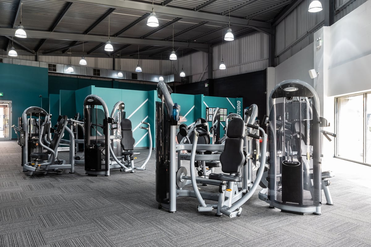 PureGym Warrington Central: Rows of resistance machines, cable stations, and adjustable benches in a dimly lit gym interior.
