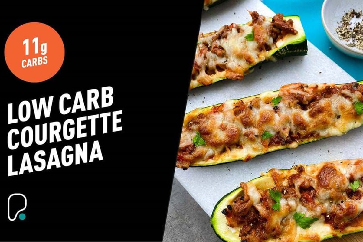 Three baked courgette halves topped with minced meat, melted cheese, and herbs on parchmen