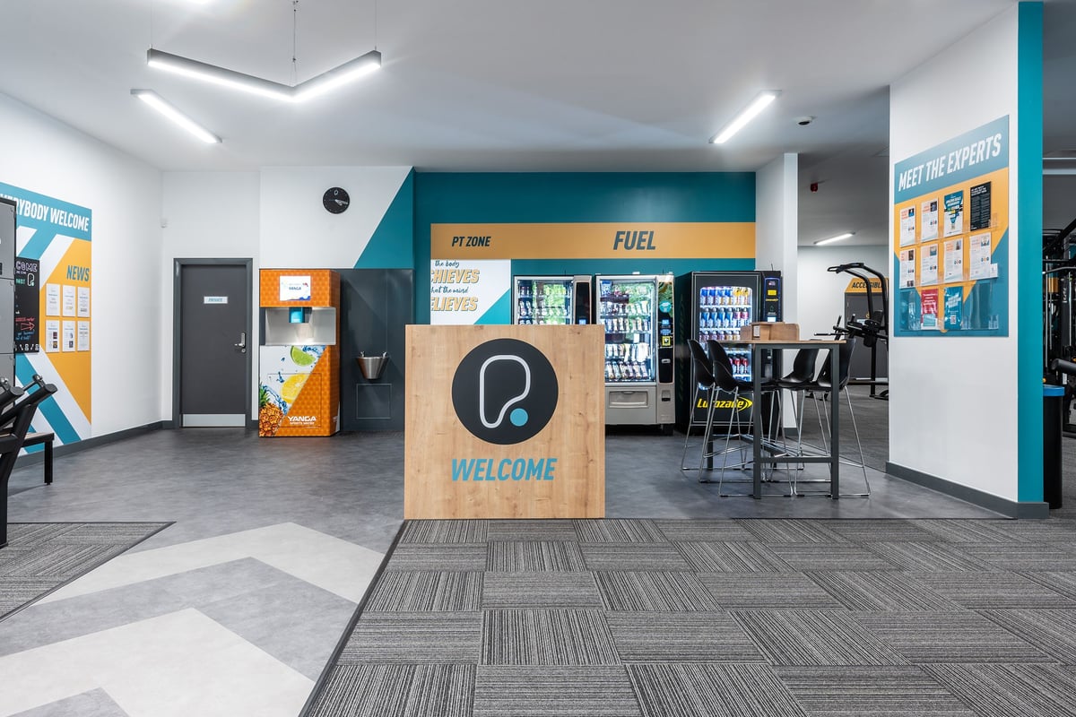 PureGym Knaesborough: Vending machines, seating area, and welcome desk in a brightly lit lobby.