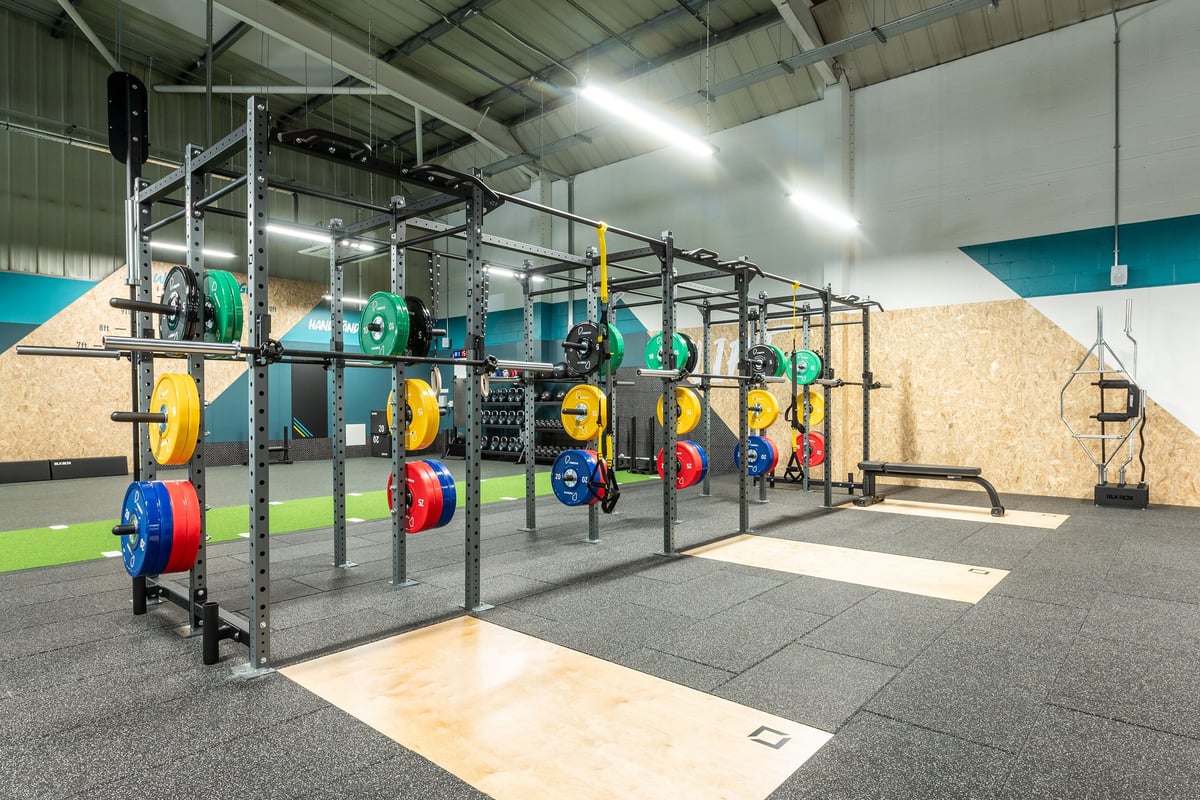 PureGym Horsham: Rig of parallel bars, weight plates in primary colours, rubberized flooring in gym setting.