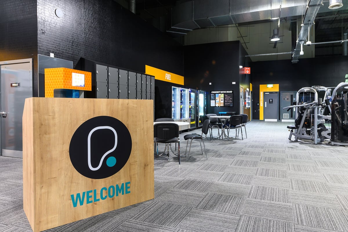 PureGym Bromborough: Lobby area with welcome signage, seating, and a modern industrial style interior design.