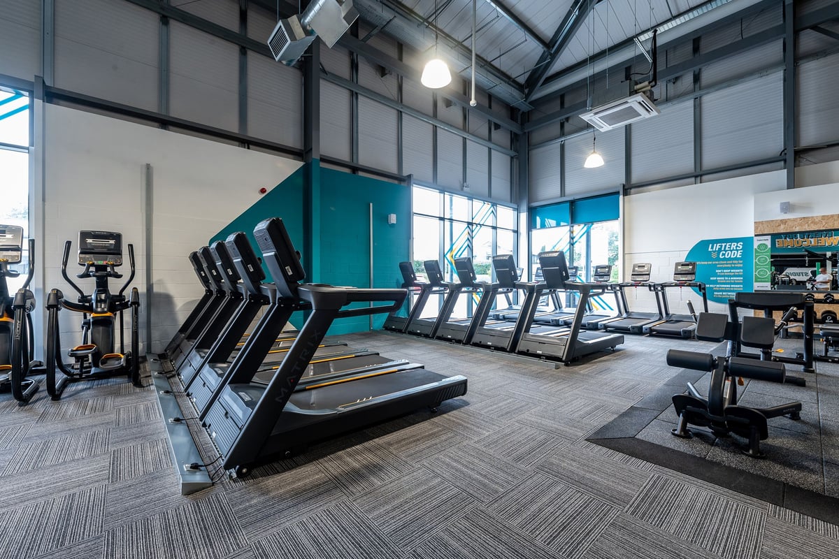 PureGym Cirencester: Rows of modern treadmills in a gym setting with vaulted ceilings and large windows.