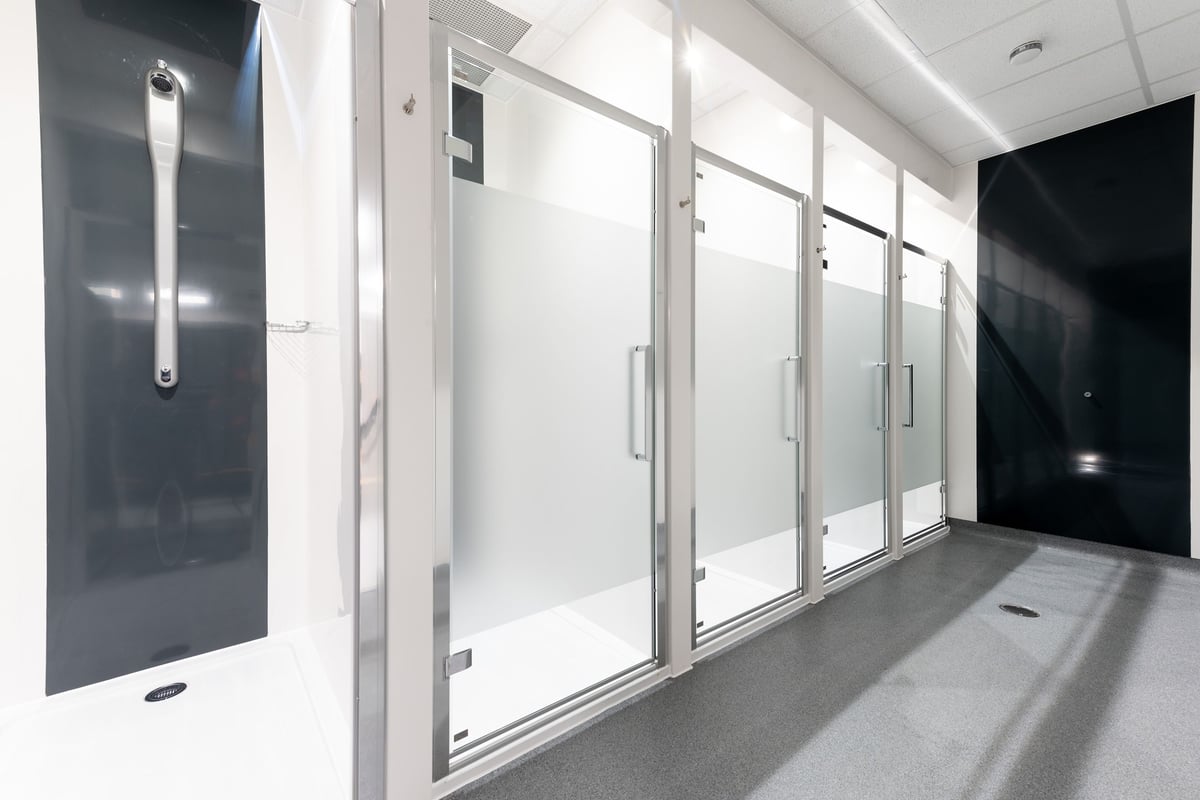 PureGym Colchester Retail Park: Glass-enclosed changing rooms with metallic handles and rubberized flooring.